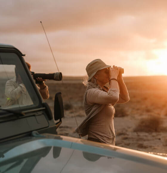 Persona che osserva gli uccelli con un binocolo accanto a un fuoristrada al tramonto alle Isole Canarie.