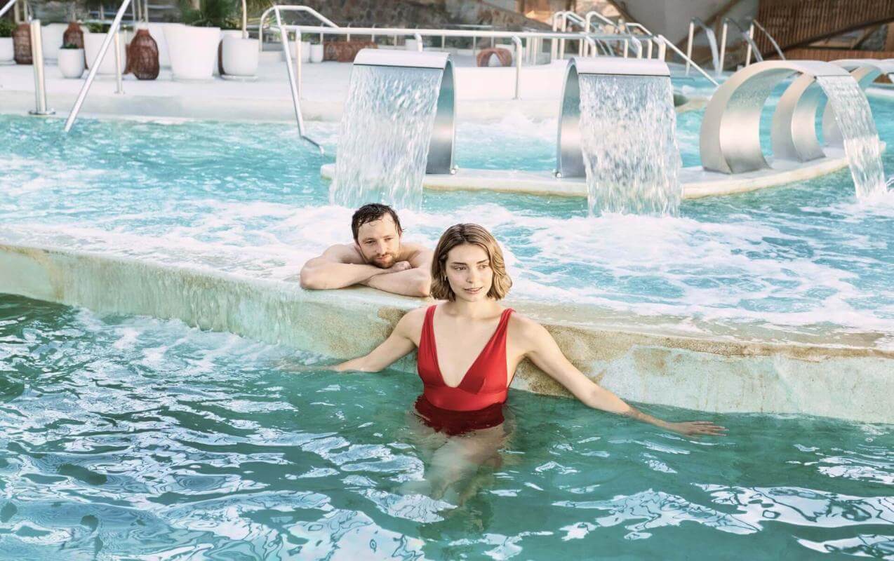 Coppia che si diverte in una piscina di talassoterapia con getti e cascate, in uno spazio progettato per il benessere e il relax.