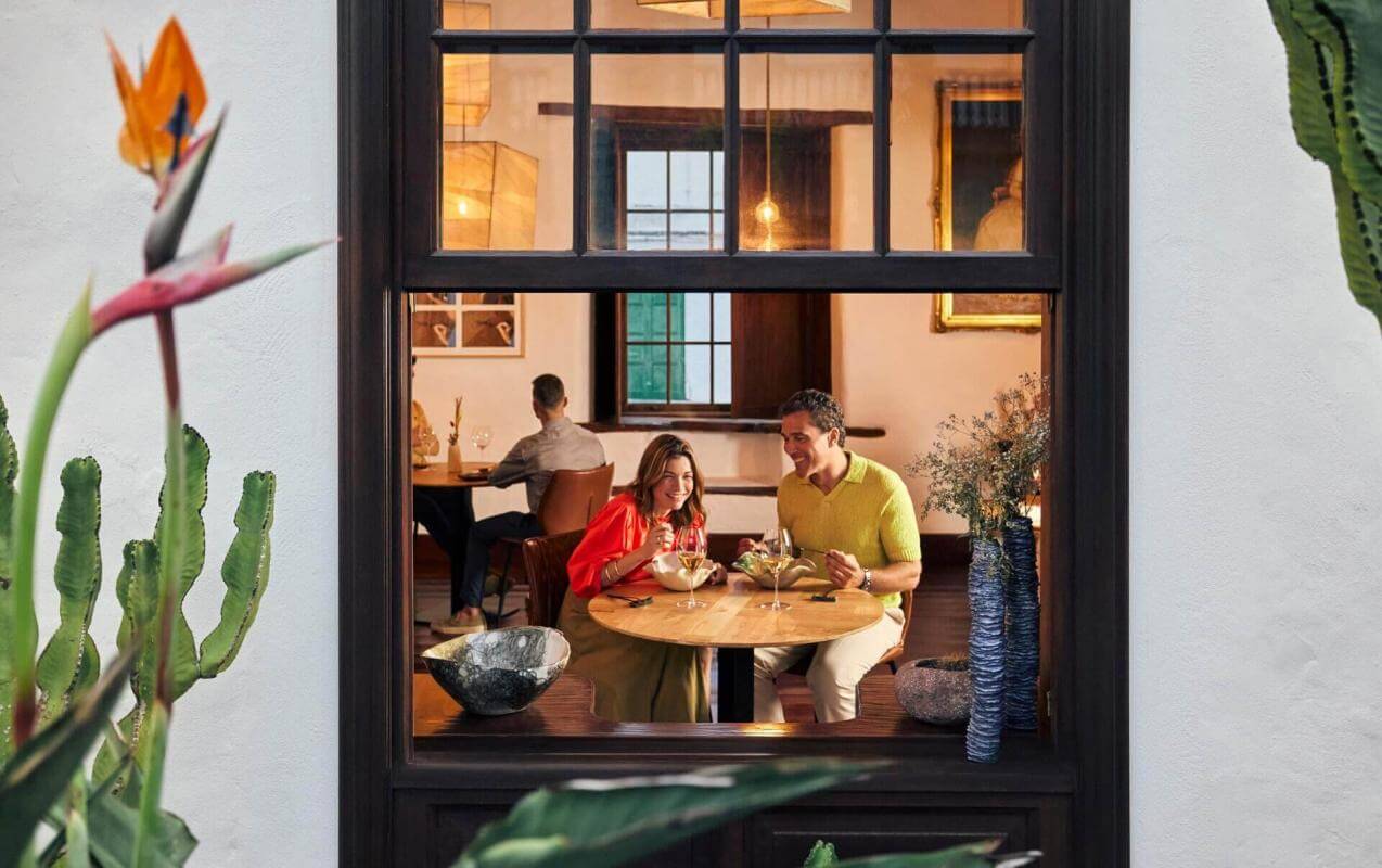 Vista dalla finestra di una coppia che mangia in un ristorante accogliente con decorazioni tradizionali e dettagli naturali.