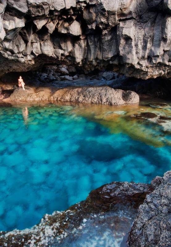 Charco Azul a El Hierro, piscina naturale con acque blu e intorno roccia vulcanica scura sotto una scogliera.