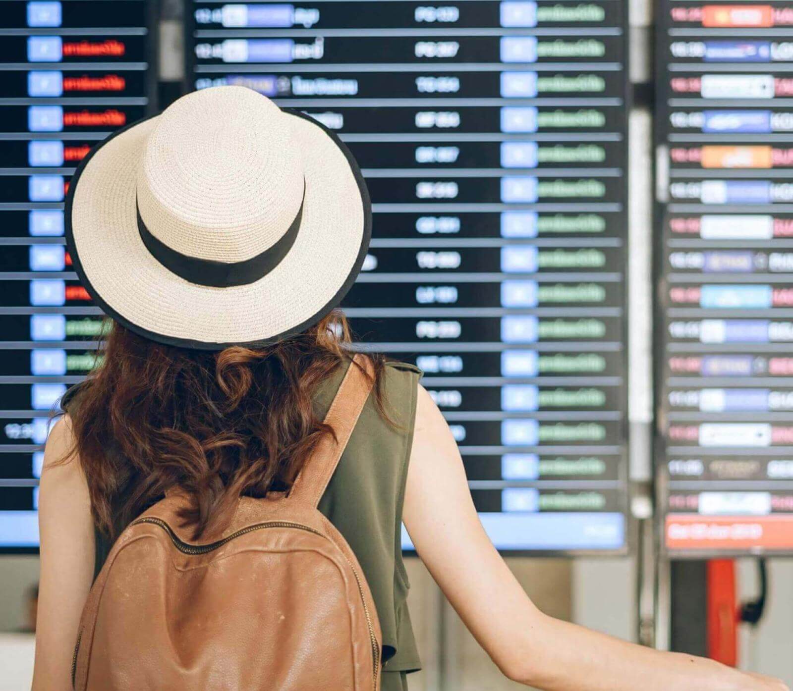 Persona con cappello e zaino che osserva il pannello delle informazioni sui voli in aeroporto.