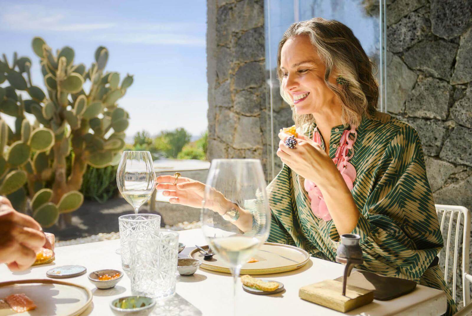 Persona che si gode un aperitivo e un bicchiere di vino su un tavolo vicino alla porta della terrazza con cactus sullo sfondo.