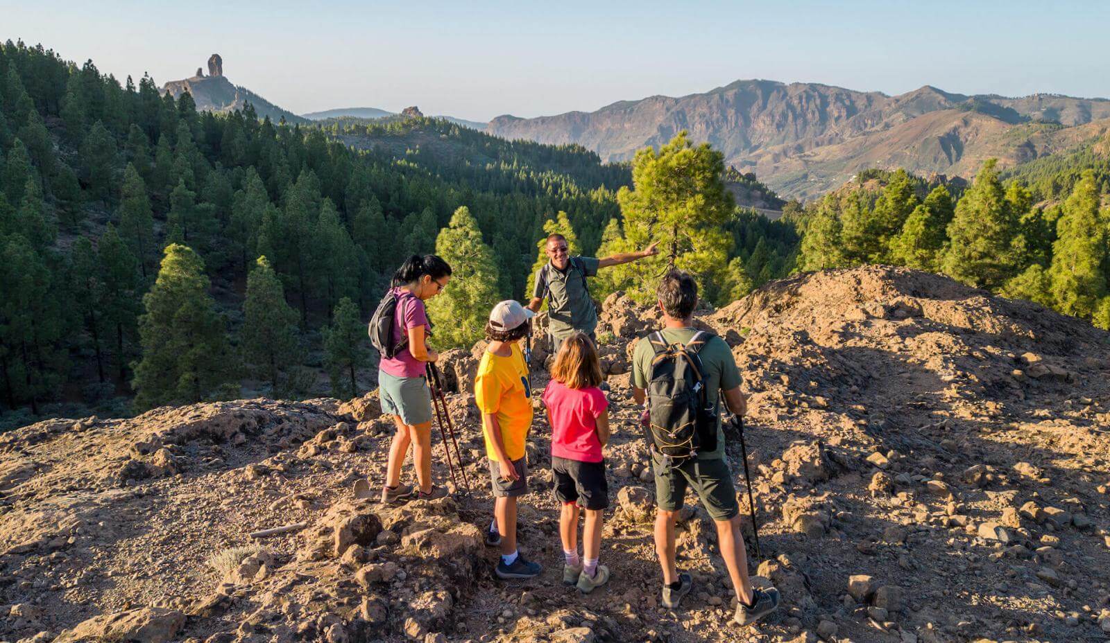 Escursione di gruppo nel Parco Rurale di Roque Nublo, tra suolo roccioso, pineta canaria e picco sullo sfondo.