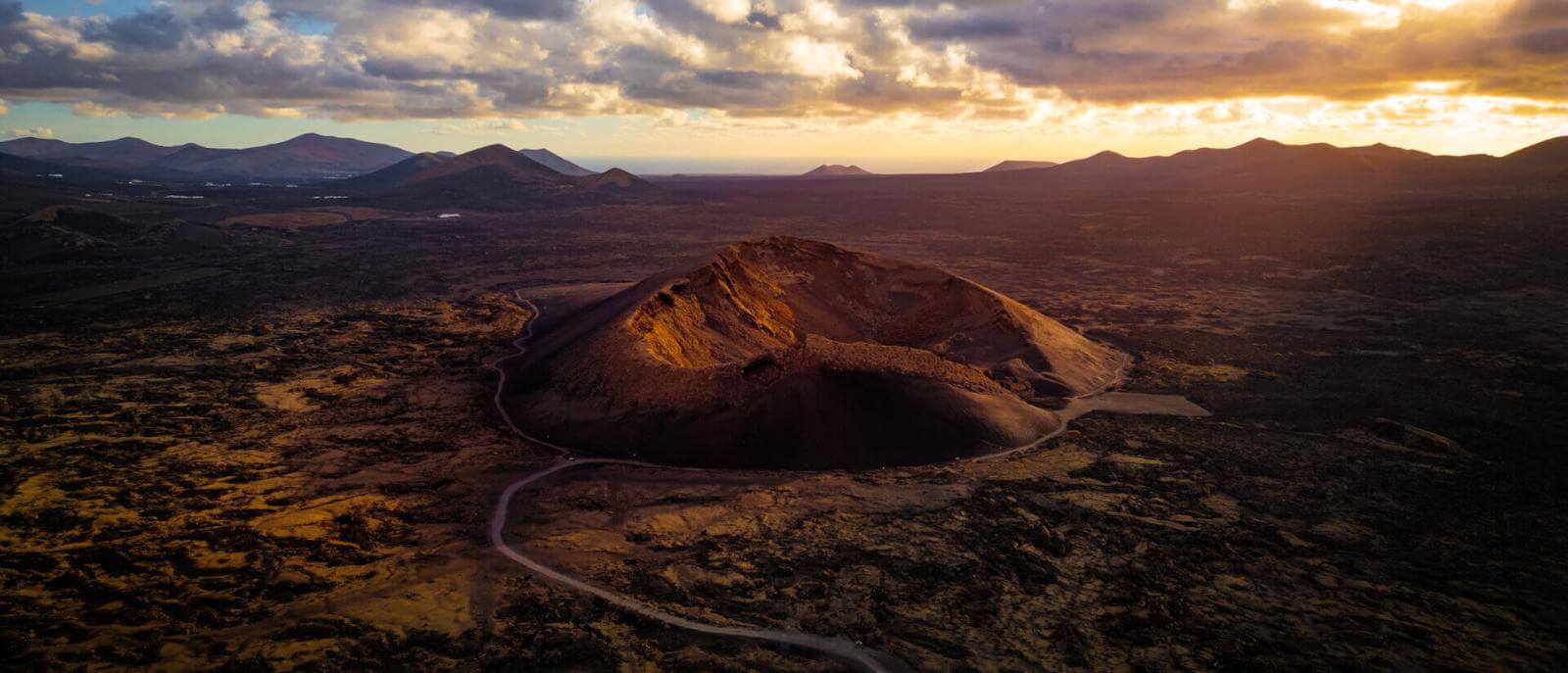 Veduta aerea del Vulcano del Cuervo a Lanzarote, con il cratere illuminato al tramonto e paesaggio vulcanico.
