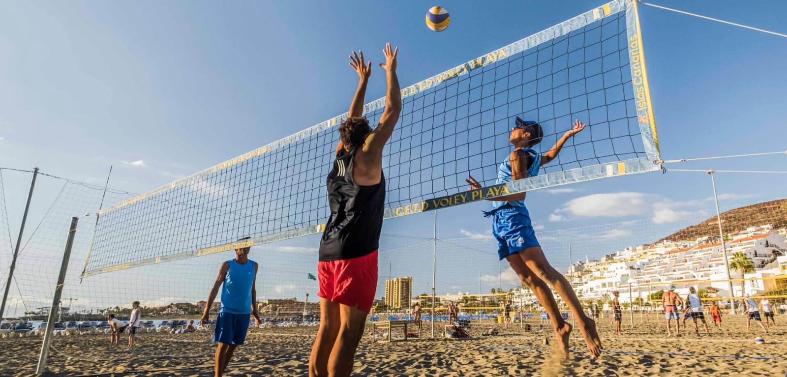 Persone che praticano beach volley e che saltano per contendersi un pallone.