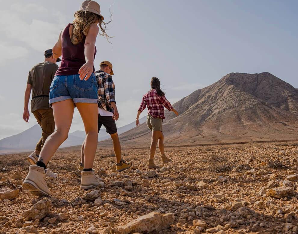 Gruppo che cammina su un terreno arido verso una montagna in un ampio paesaggio naturale.