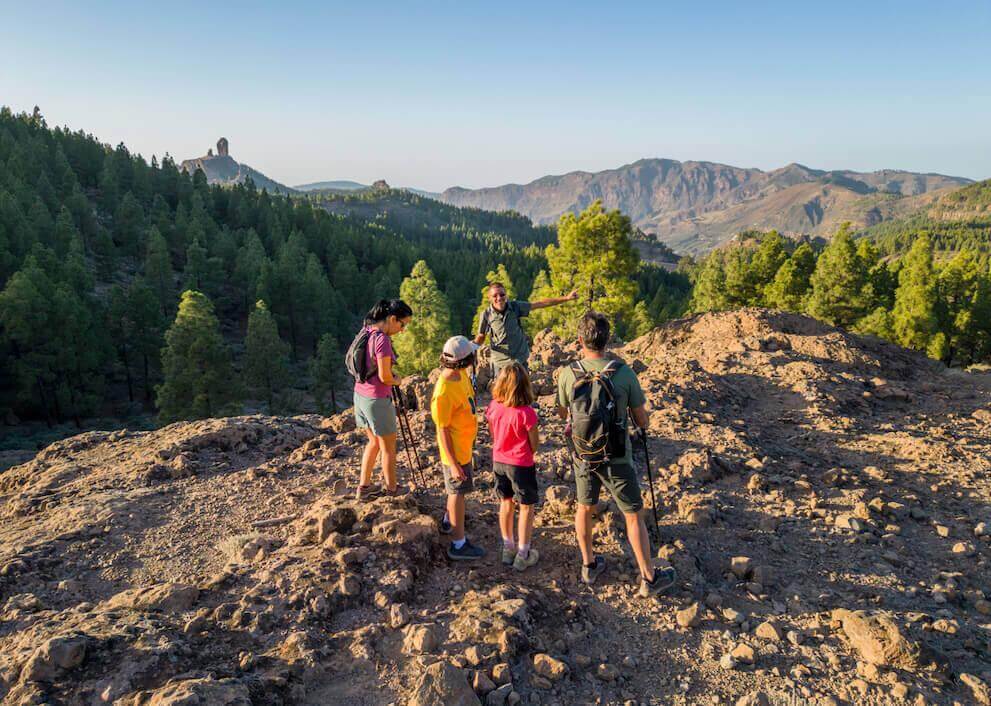 Escursione di gruppo nel Parco Rurale di Roque Nublo, tra suolo roccioso, pineta canaria e picco sullo sfondo.
