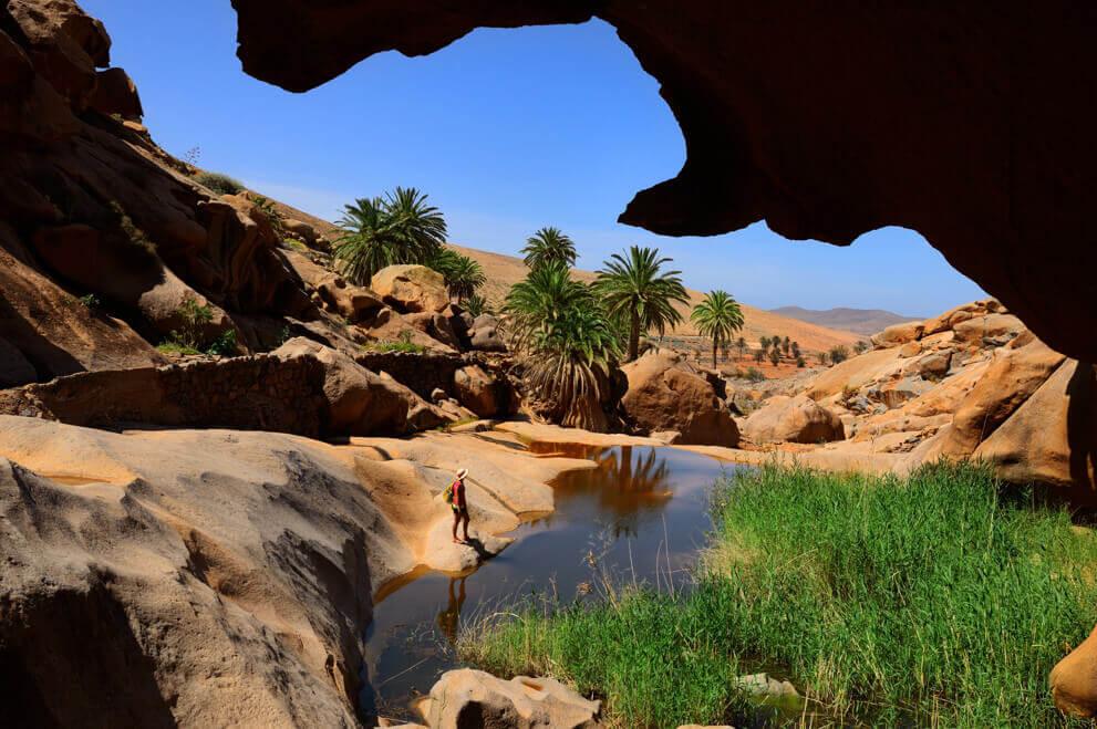 Gola di Las Peñitas a Fuerteventura, con rocce, palme e una piccola piscina in un paesaggio arido.