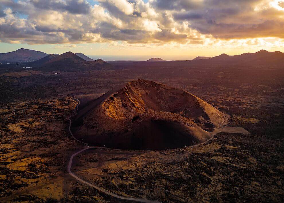 Veduta aerea del Vulcano del Cuervo a Lanzarote, con il cratere illuminato al tramonto e paesaggio vulcanico.