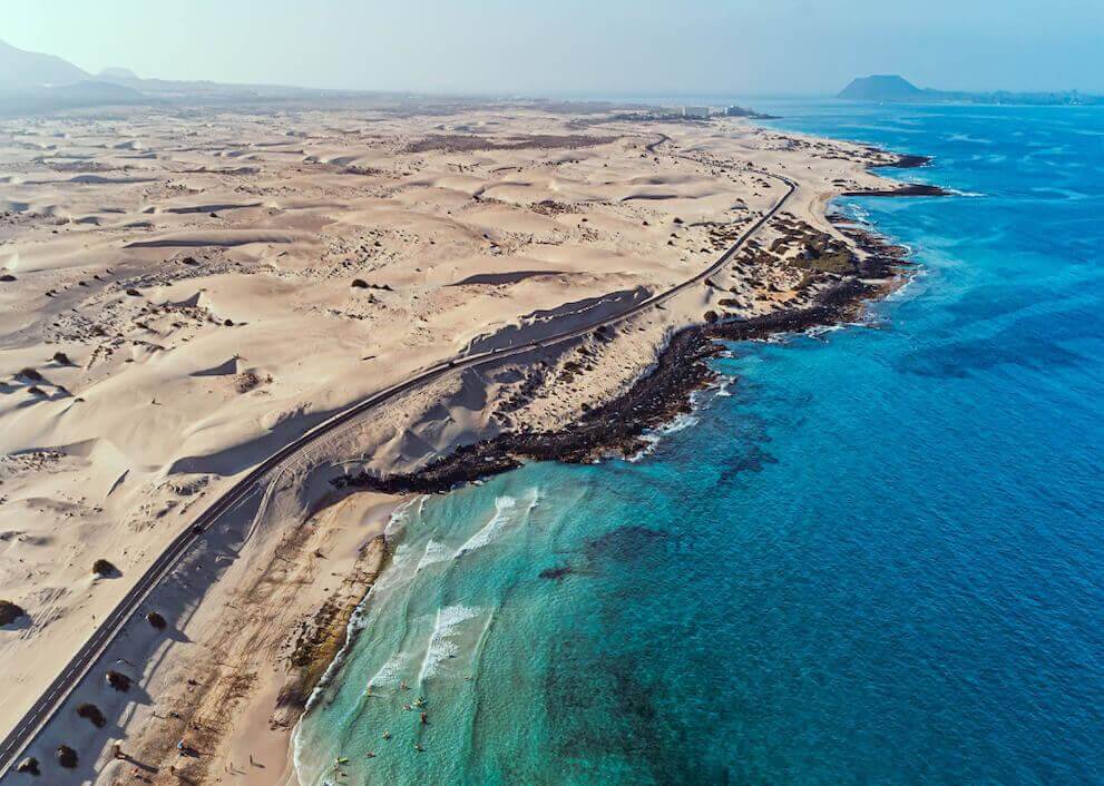 Vista aerea delle Dune di Corralejo a Fuerteventura, con ampi arenili su mare turchese e costa vulcanica.