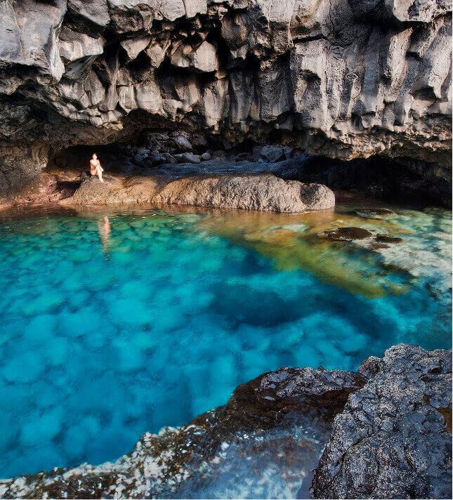 Charco Azul a El Hierro, piscina naturale con acque blu e intorno roccia vulcanica scura sotto una scogliera.