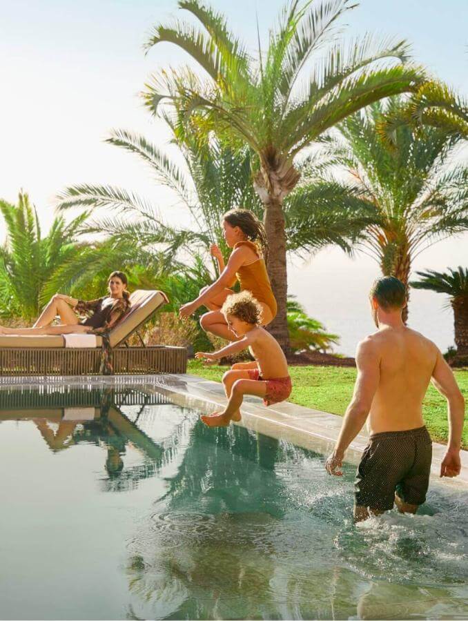Famiglia che si rilassa in una piscina a sfioro circondata da palme e prati, in un ambiente soleggiato con viste naturali.