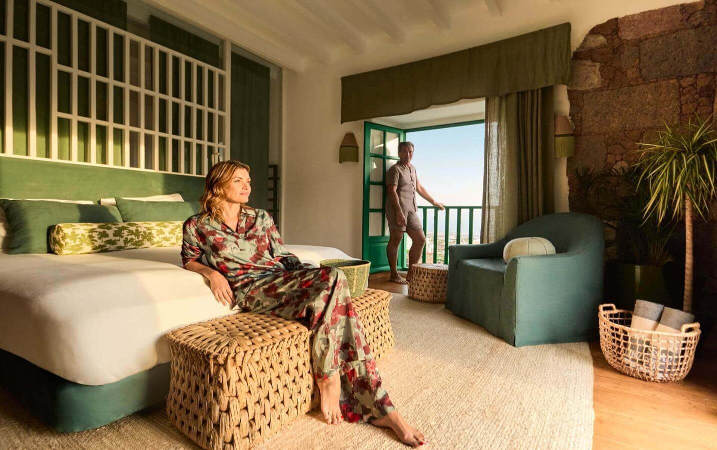 Persona rilassata in camera con arredi dai toni verdi e terrazza aperta sul paesaggio, in un'atmosfera calda e accogliente.