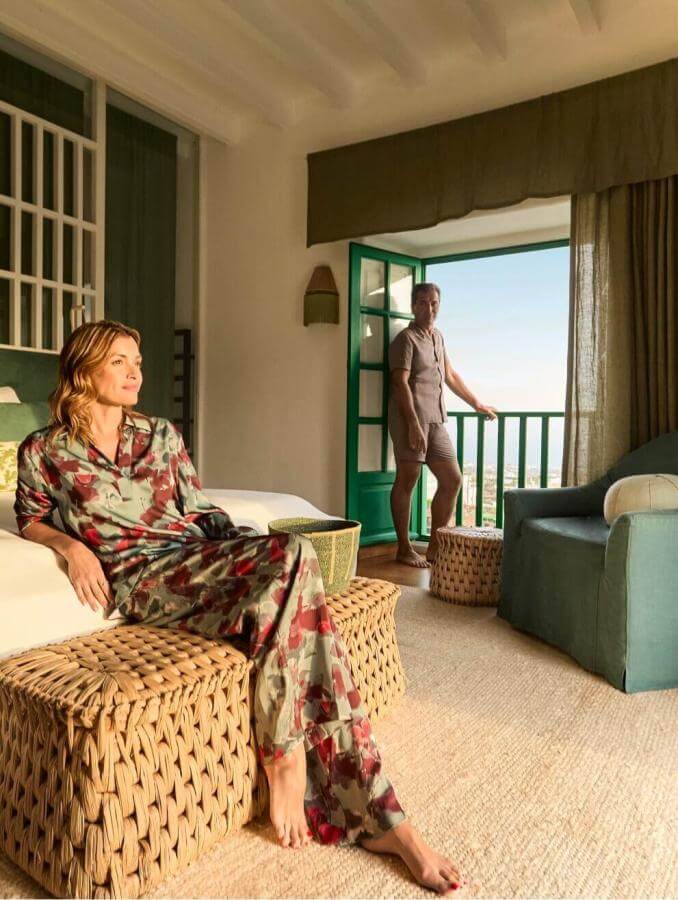 Persona rilassata in camera con arredi dai toni verdi e terrazza aperta sul paesaggio, in un'atmosfera calda e accogliente.