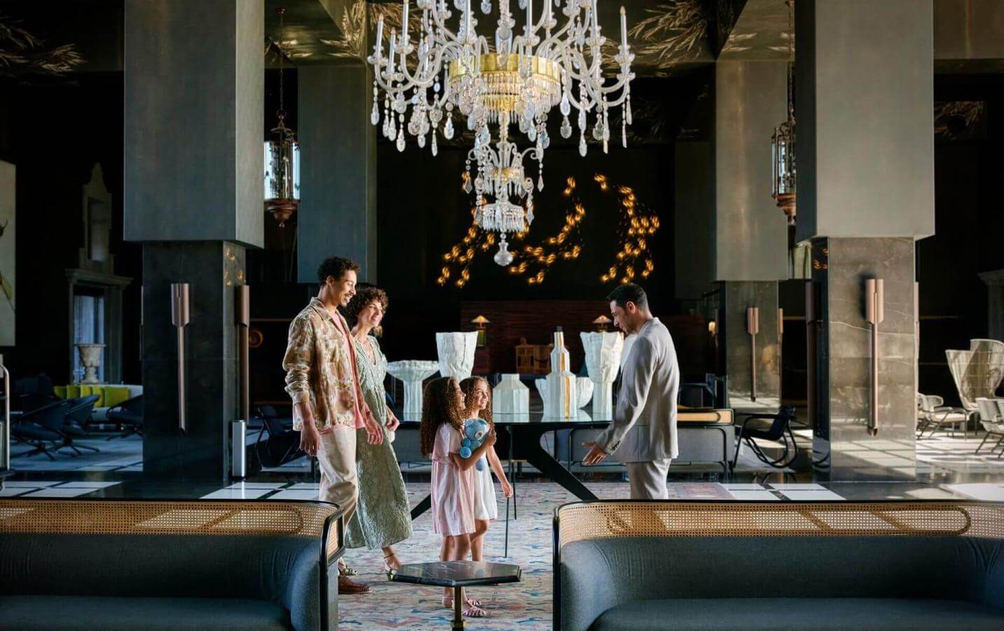 Famiglia in arrivo in hotel elegante con lampada in vetro e arredi sofisticati, in spazi ampi dal design contemporaneo.