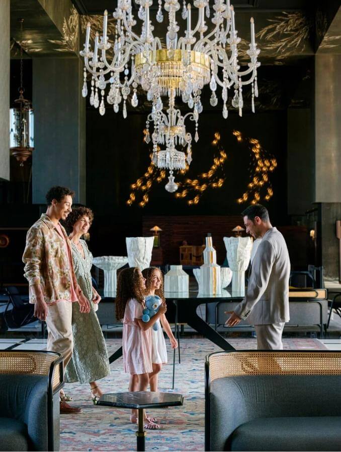 Famiglia in arrivo in hotel elegante con lampada in vetro e arredi sofisticati, in spazi ampi dal design contemporaneo.