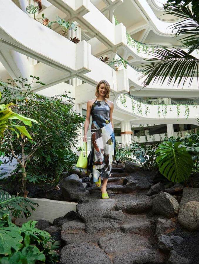 Persona che cammina lungo un sentiero circondato da vegetazione tropicale al coperto con architettura bianca e design organico.