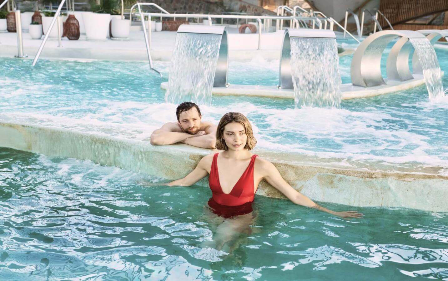 Coppia che si diverte in una piscina di talassoterapia con getti e cascate, in uno spazio progettato per il benessere e il relax.