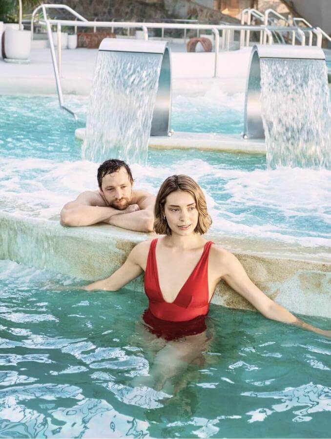 Coppia che si diverte in una piscina di talassoterapia con getti e cascate, in uno spazio progettato per il benessere e il relax.