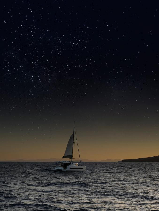 Barca a vela che naviga al tramonto sotto il cielo stellato in acque calme, creando un'esperienza unica in mare.
