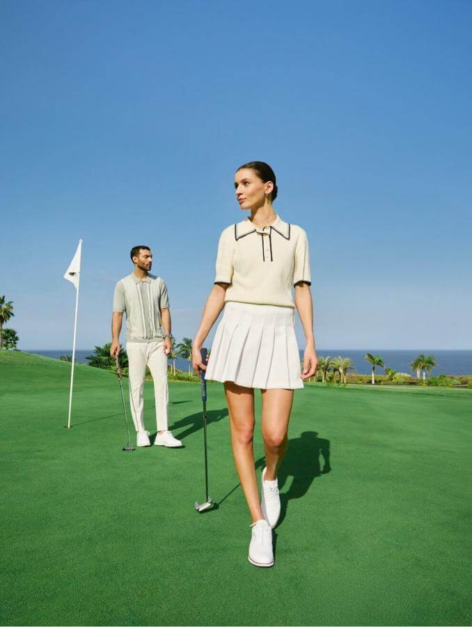 Persone che giocano a golf in un campo verde in riva al mare con bandiera nella buca e cielo limpido.