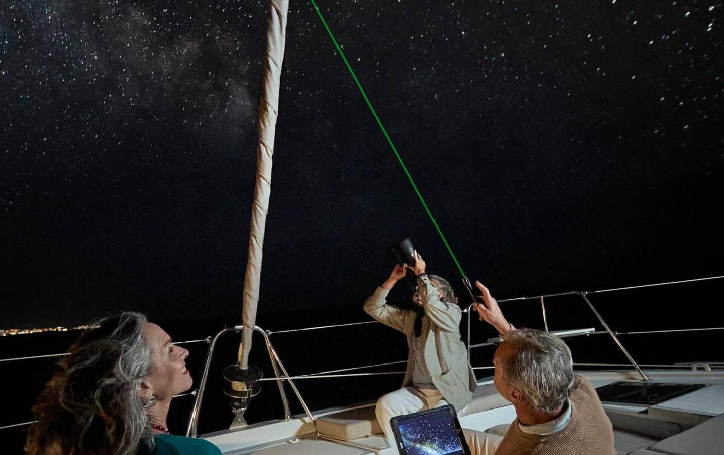 Osservazione astronomica da una barca a vela sotto il cielo stellato con puntatore laser nelle calme acque dell'oceano.
