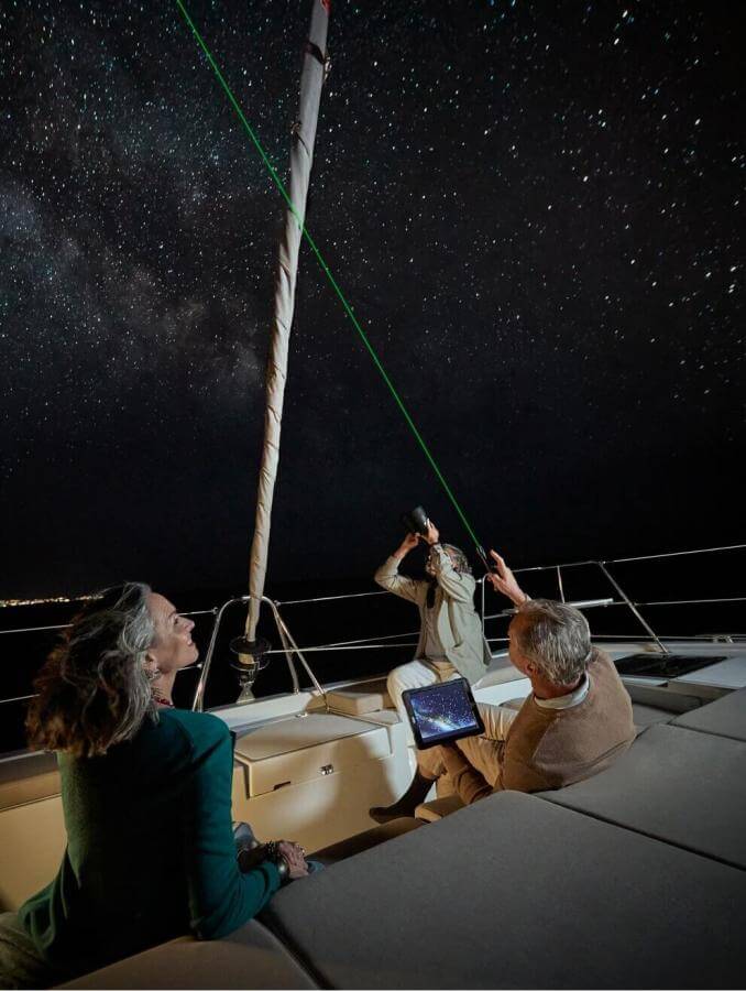 Osservazione astronomica da una barca a vela sotto il cielo stellato con puntatore laser nelle calme acque dell'oceano.